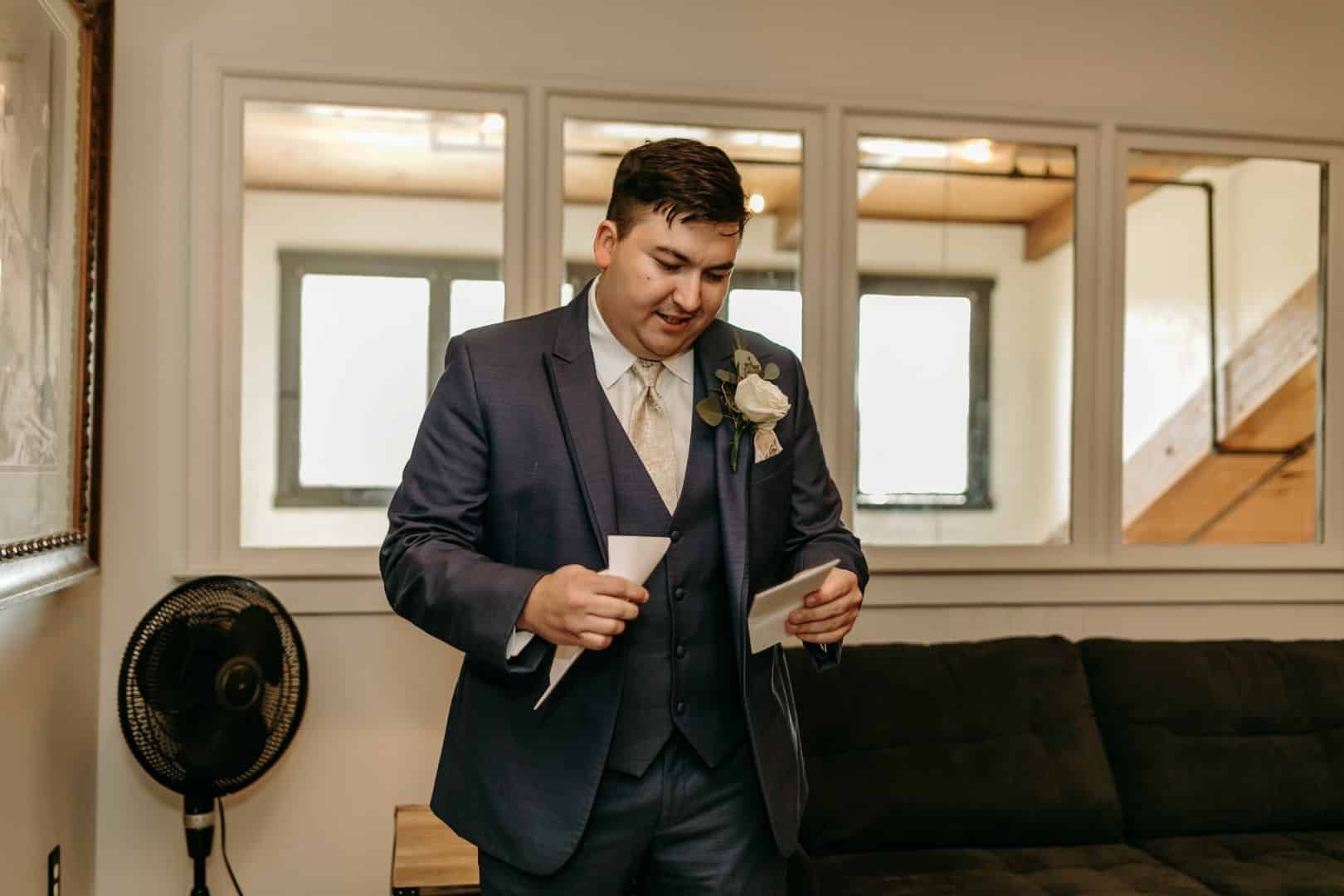 A man in a suit is standing in a living room holding a piece of paper.