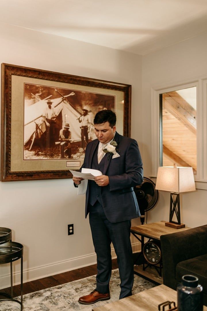 A man in a suit is reading a letter in a living room.