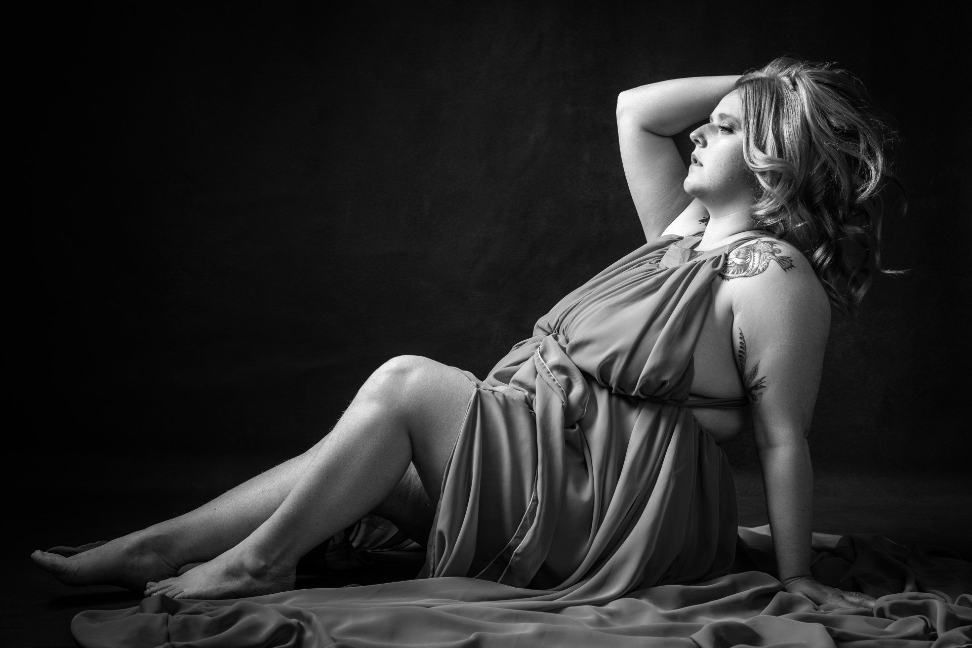 black and white boudoir portrait of woman sitting on floor wearing flowy gown