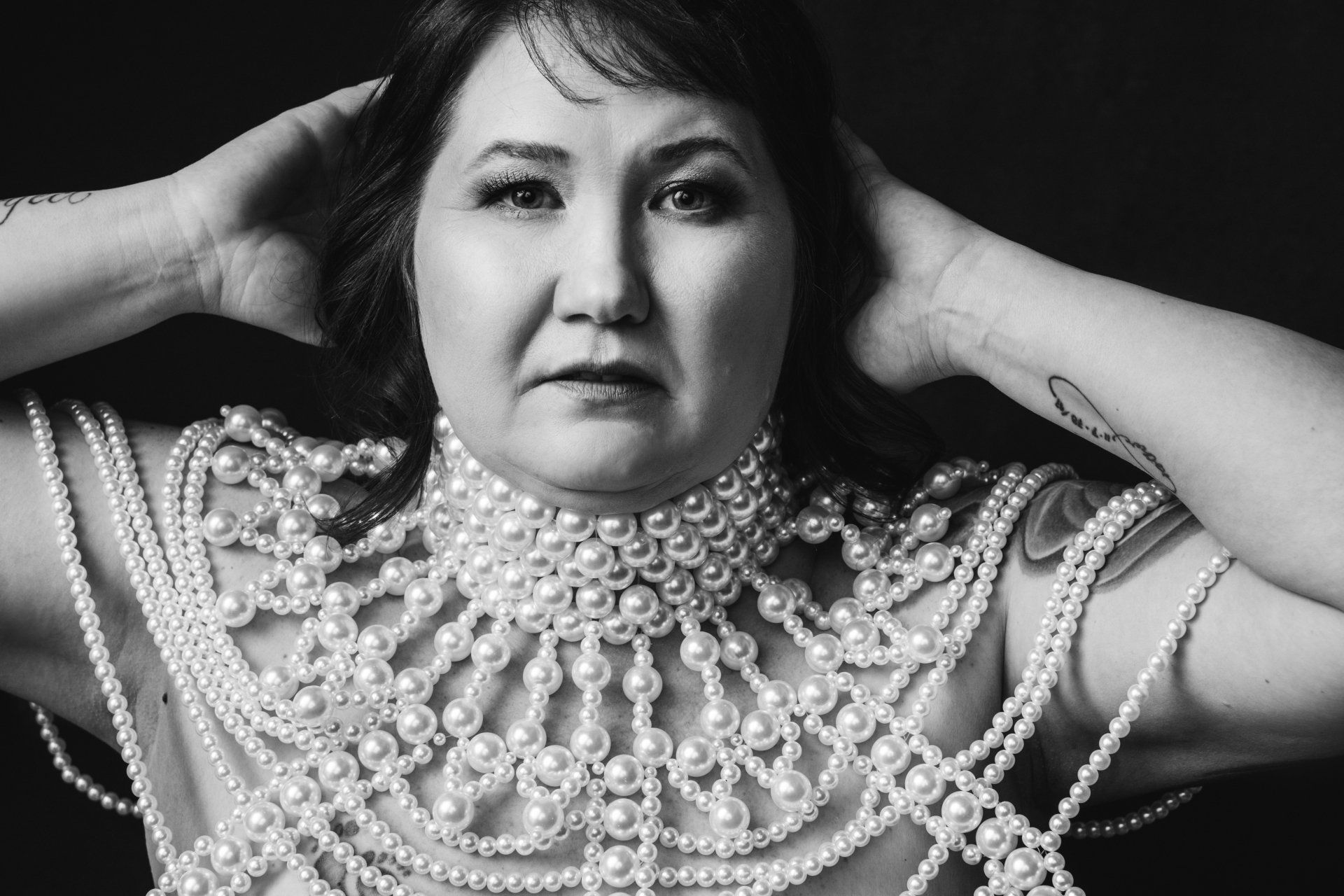 boudoir portrait of a woman in an elaborate pearl necklace with her hands on her head