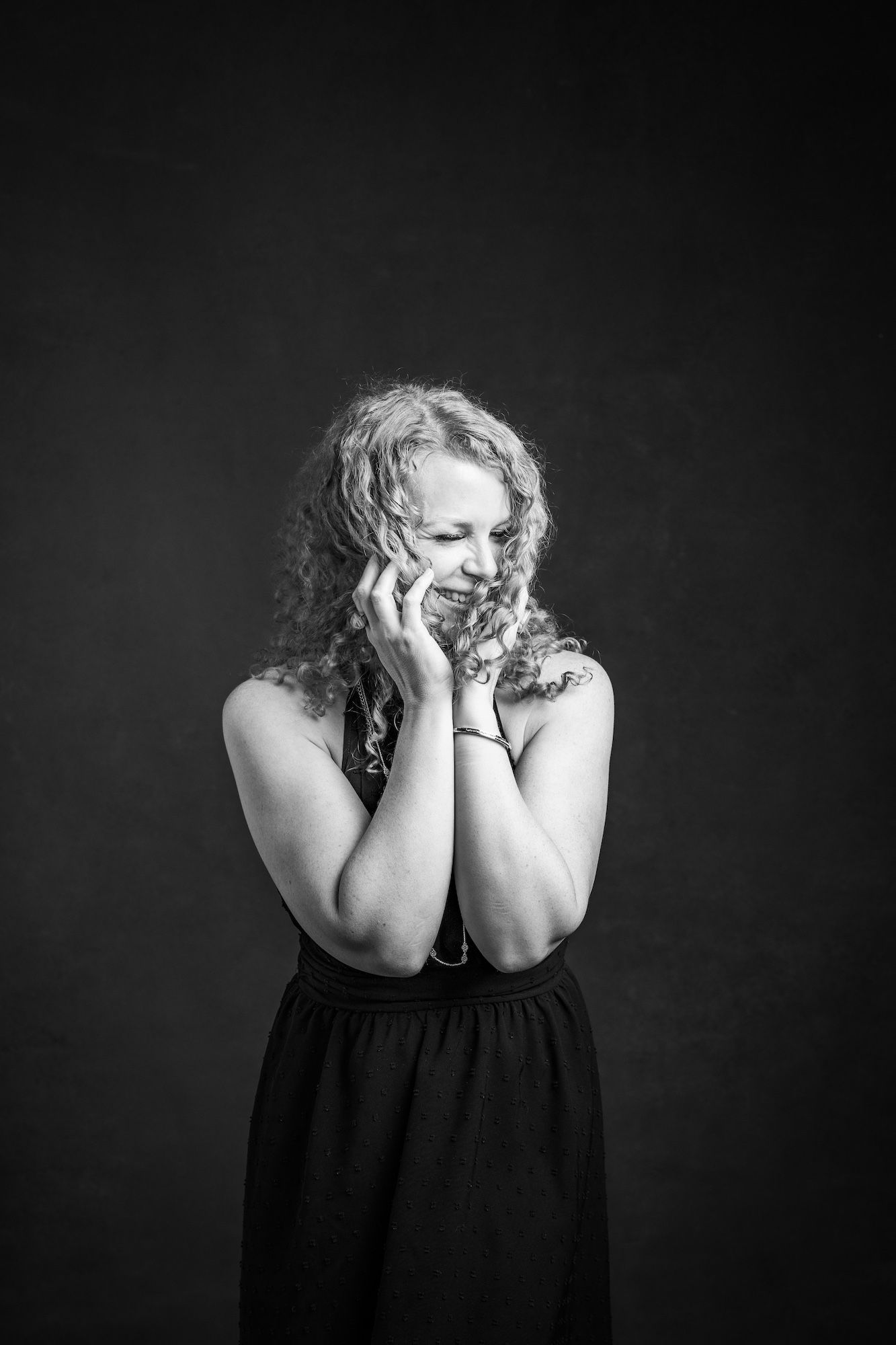 A woman in a black dress, with hands covering her face.