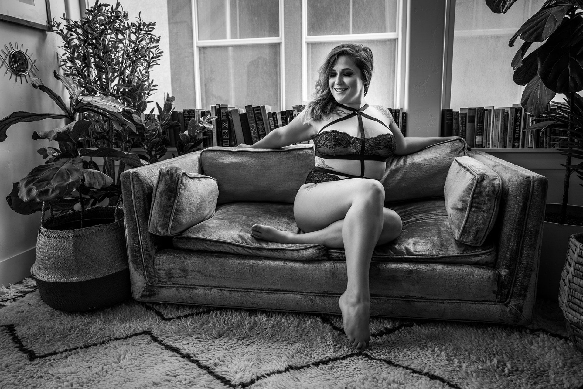 woman sitting on a couch in a lingerie looking away and smiling during a boudoir session