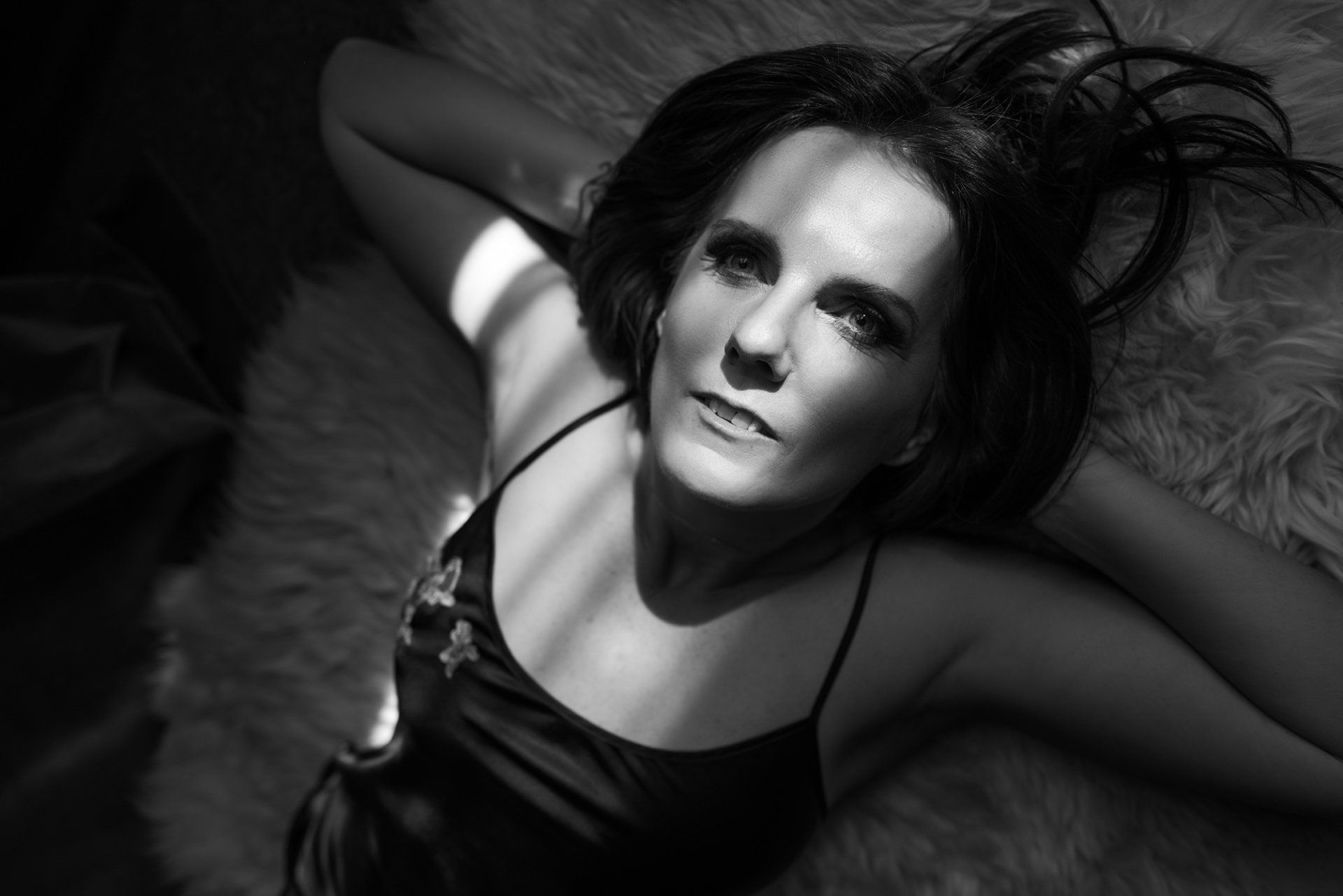 boudoir portrait of woman lying on rug with hands behind head and light caressing her face