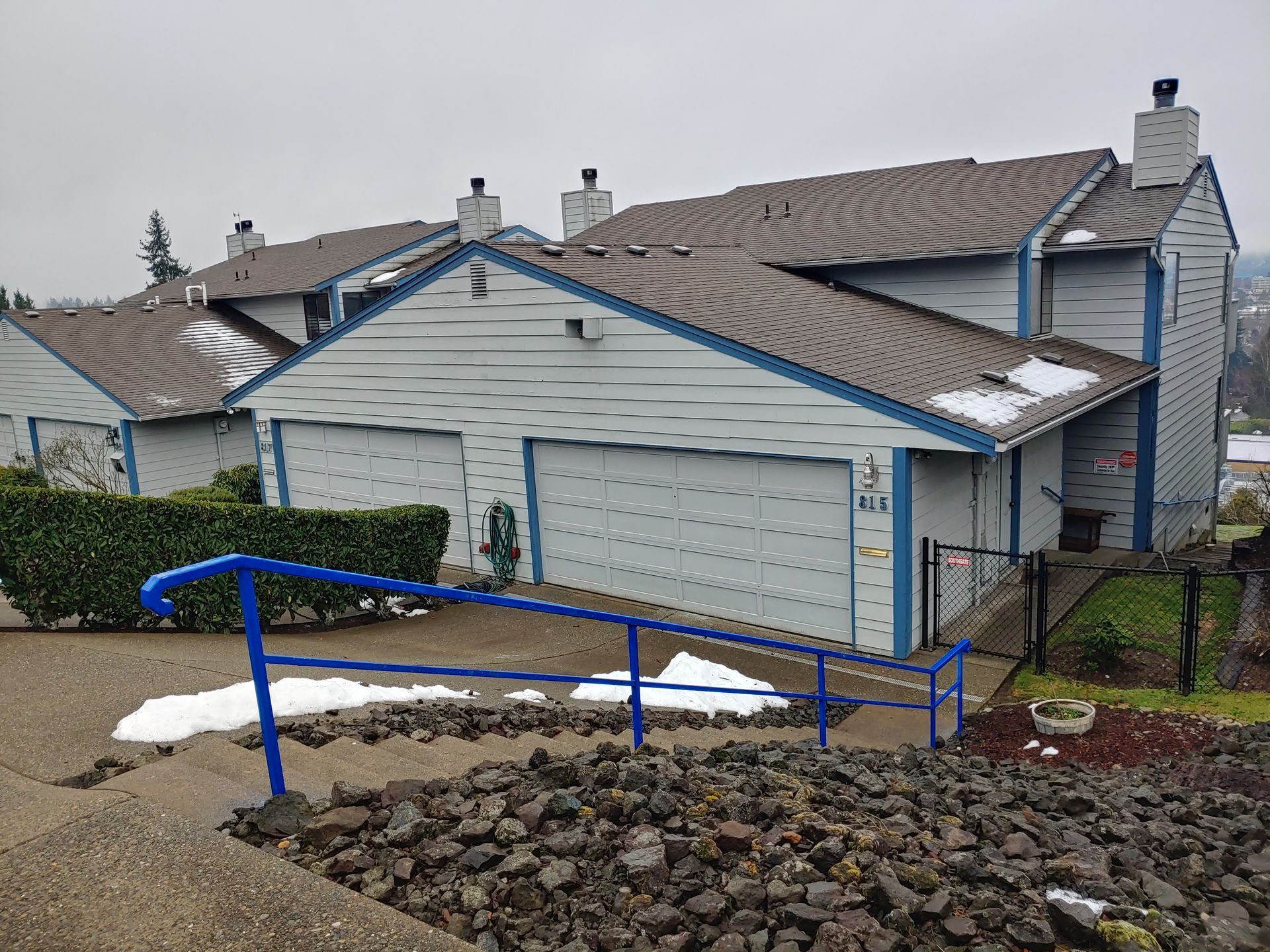 Townhouses with blue trim, a blue handrail, and snow on the roof and stairs.