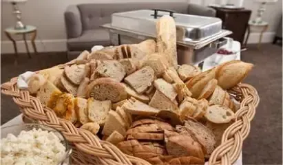 Basket of assorted sliced bread on a buffet table with a chafing dish in the background