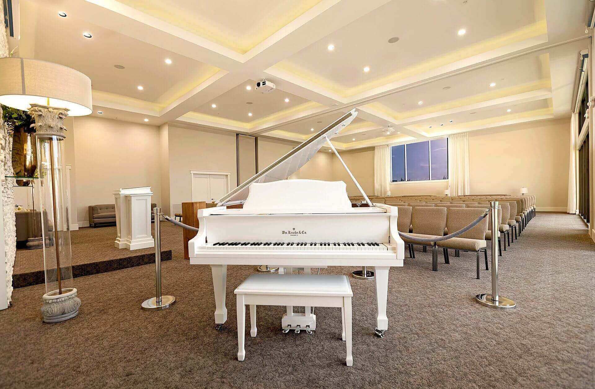 White grand piano in a spacious beige hotel lounge with seating and a polished ceiling