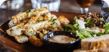 Grilled chicken with roasted potatoes, dipping sauce, and salad on a wooden table
