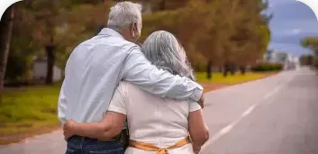 Two people walking arm in arm on a tree-lined road, viewed from behind.