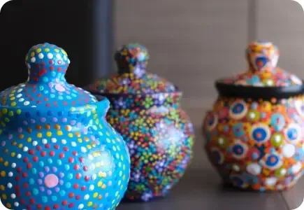 Three colorful, dot-covered ceramic jars on a tabletop, with blue, multicolored, and orange patterns.
