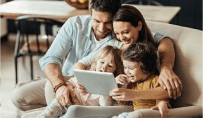 Family smiling and using a tablet together on a couch in a cozy living room