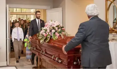 Mourners carrying a flower-covered casket through a doorway in a funeral procession