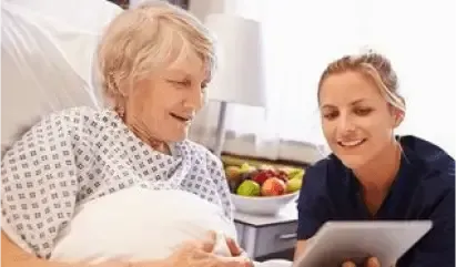 Older woman in hospital bed smiling with a nurse holding a tablet nearby
