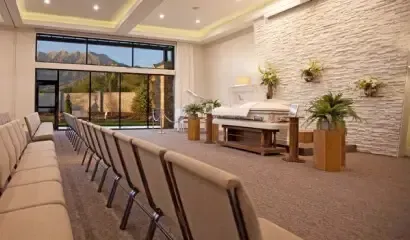 Modern chapel with rows of chairs, altar, and stone accent wall, lit by large windows and warm ceiling lights