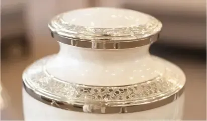 Close-up of a white ceramic jar with ornate silver trim on the lid and body