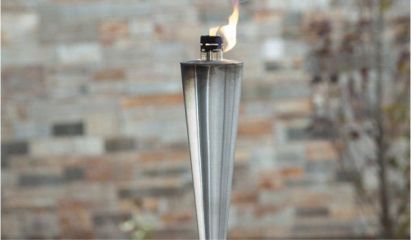 Lit metal tiki torch with a small flame against a brick wall backdrop