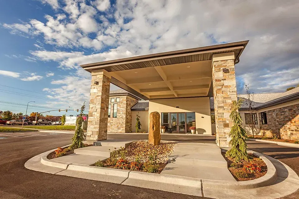 Stone entrance canopy with columns and landscaping at a building driveway under a blue sky