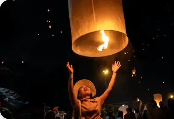 People releasing glowing lanterns at night, with one large lantern lit overhead and hands raised below.