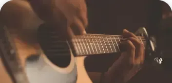 Close-up of hands playing an acoustic guitar in warm, dim light