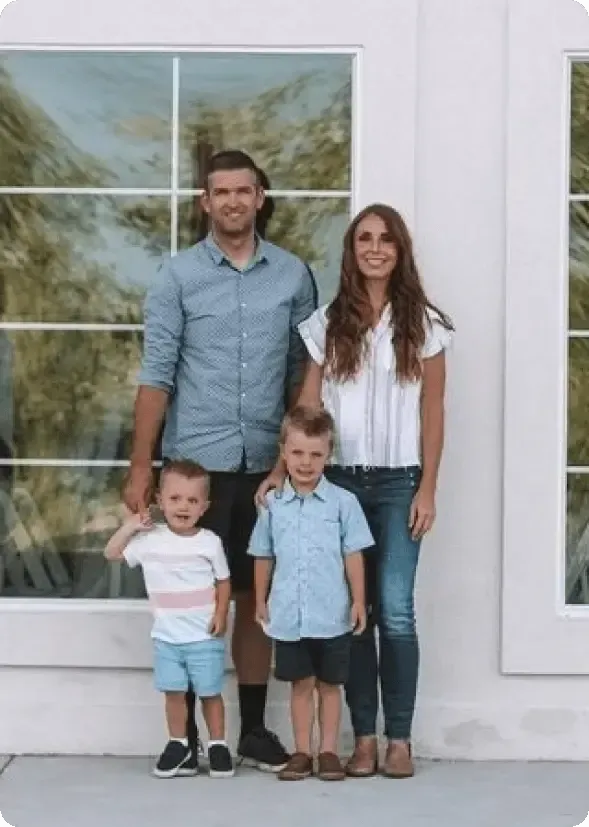 Family of four standing outside a white house in front of a glass-paneled door.