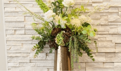 Floral arrangement with white and green flowers on tall brass stands against a light stone wall