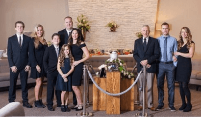 Group posed indoors at a formal event beside a wooden memorial table with flowers and a rope barrier