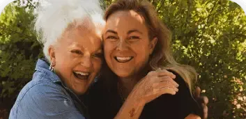 Two smiling people hugging outdoors in warm sunlight