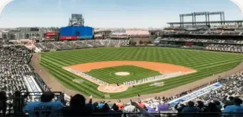 Wide view of a baseball stadium with a green field, empty stands, and city skyline beyond the outfield