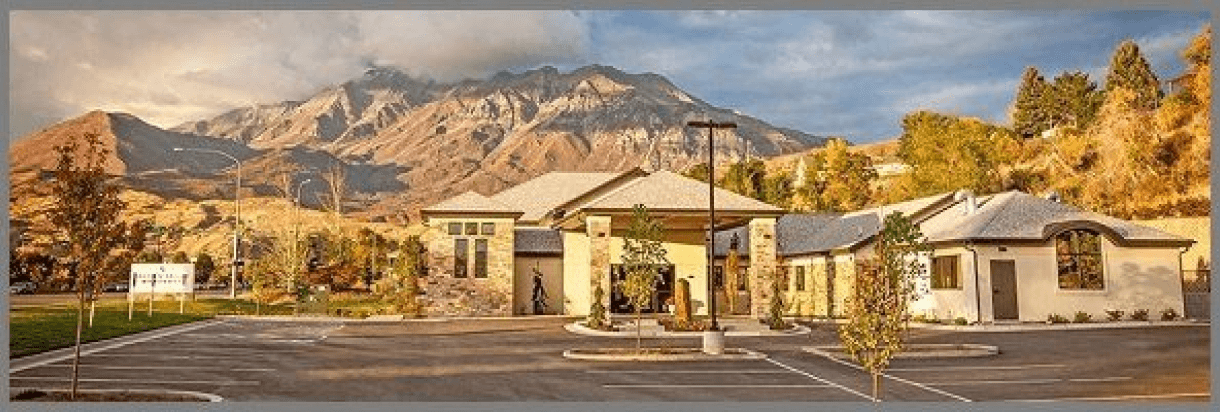 Mountain lodge entrance with cabins, autumn trees, and snow-capped peaks in the background