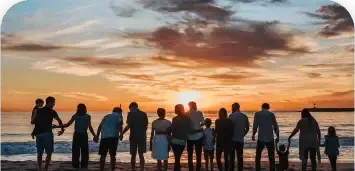 Silhouetted group holding hands on a beach at sunset, facing the ocean