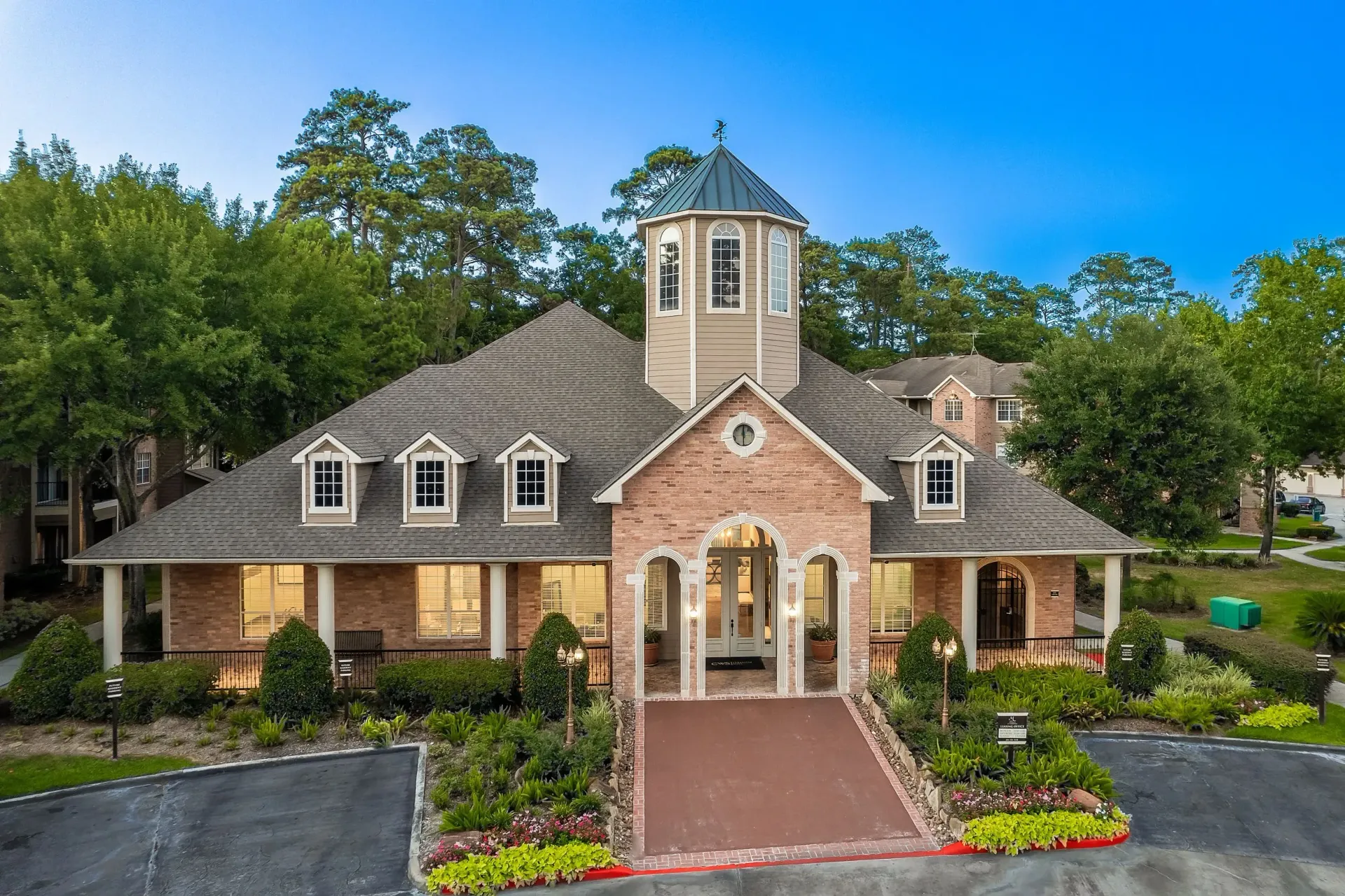 Exterior of a brick apartment building with a cupola and landscaped grounds.