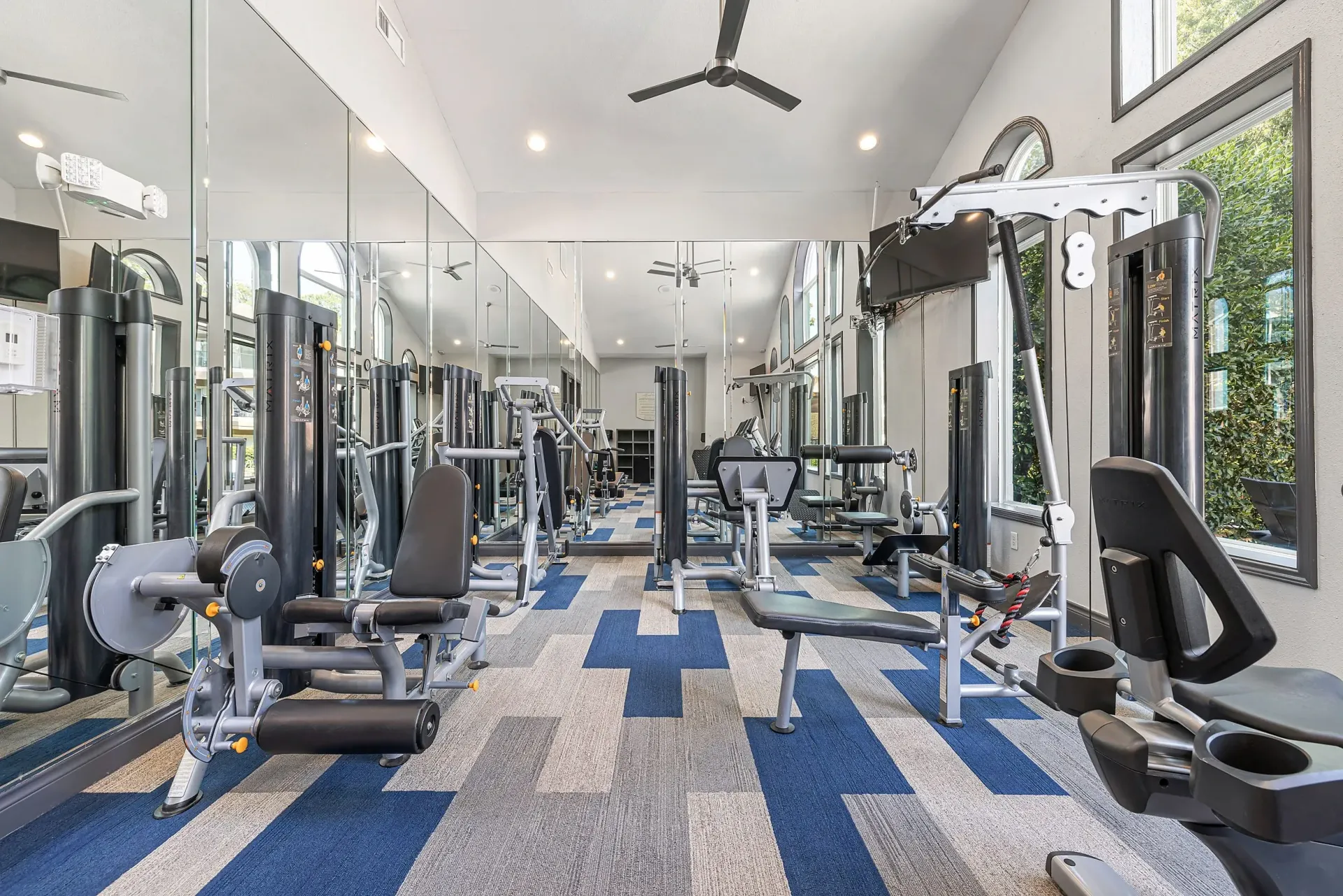 Fully equipped gym with weight machines and treadmills, large mirrors, and modern carpet.