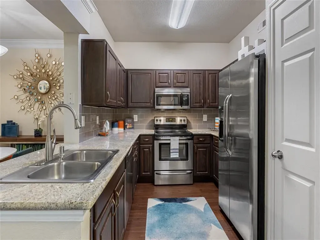 Modern kitchen with dark wood cabinets, stainless steel appliances, granite countertops, and a double sink.