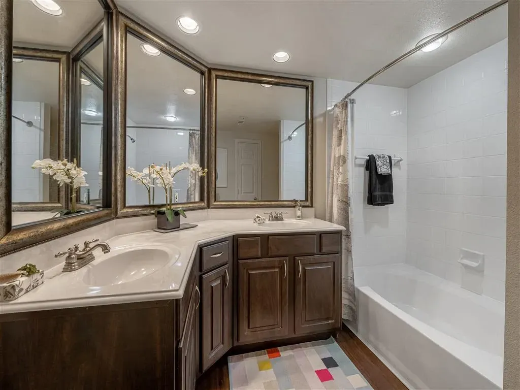 Bathroom vanity with double sinks, large mirrors, and a bathtub with white tiled walls.