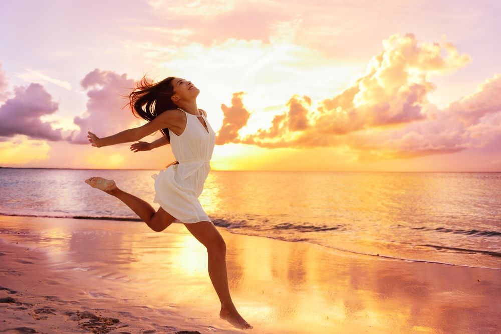 A Woman Is Jumping in The Air on The Beach at Sunset — Moving Beyond OK In Mount Warren Park, QLD
