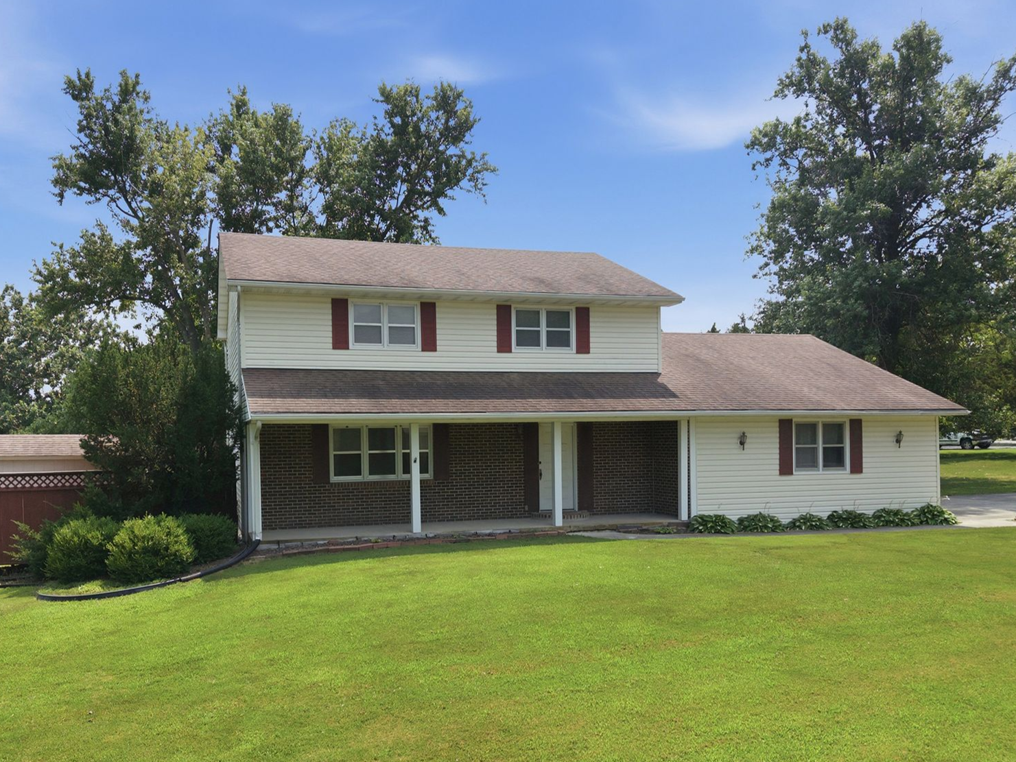 Two-story suburban house with white siding, front porch, and large green lawn under a blue sky