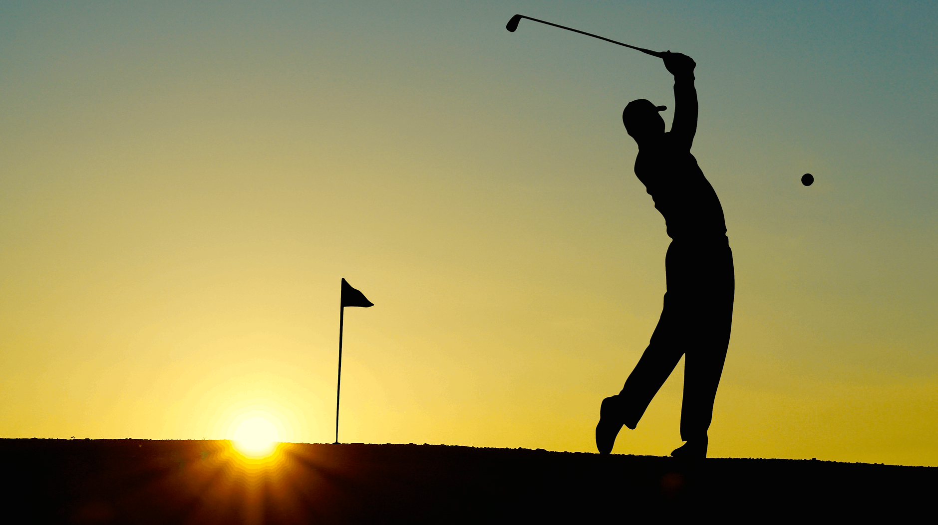 A silhouette of a man swinging a golf club at sunset