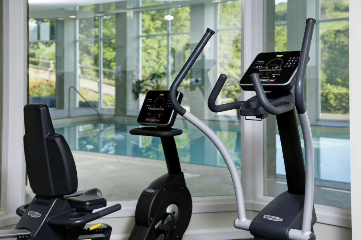 Two exercise bikes are in a gym next to a swimming pool