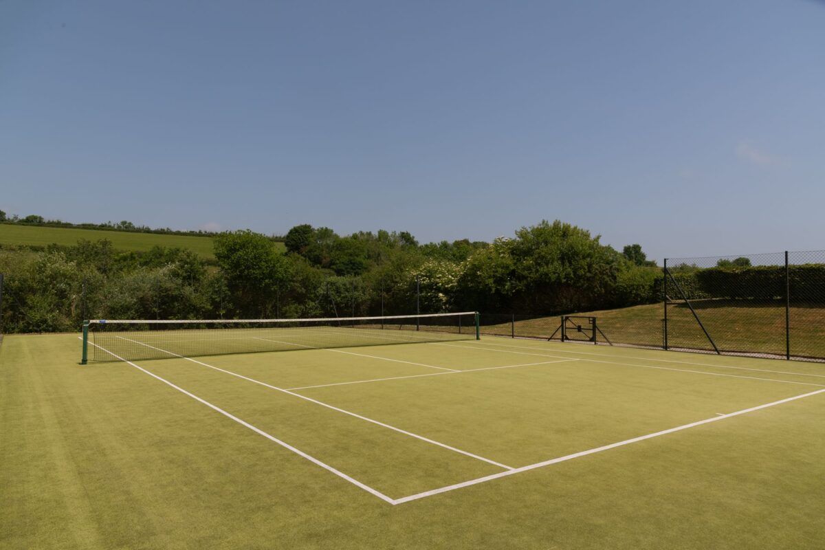 There is a tennis court in the middle of a field.