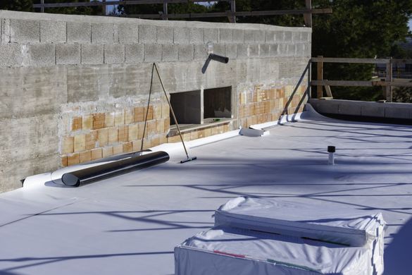 Flat roof construction with white membrane, near a concrete block wall and two window openings.