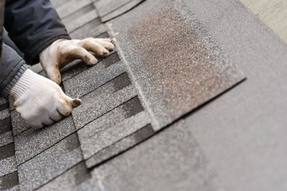 Hands in work gloves placing asphalt roof shingles.