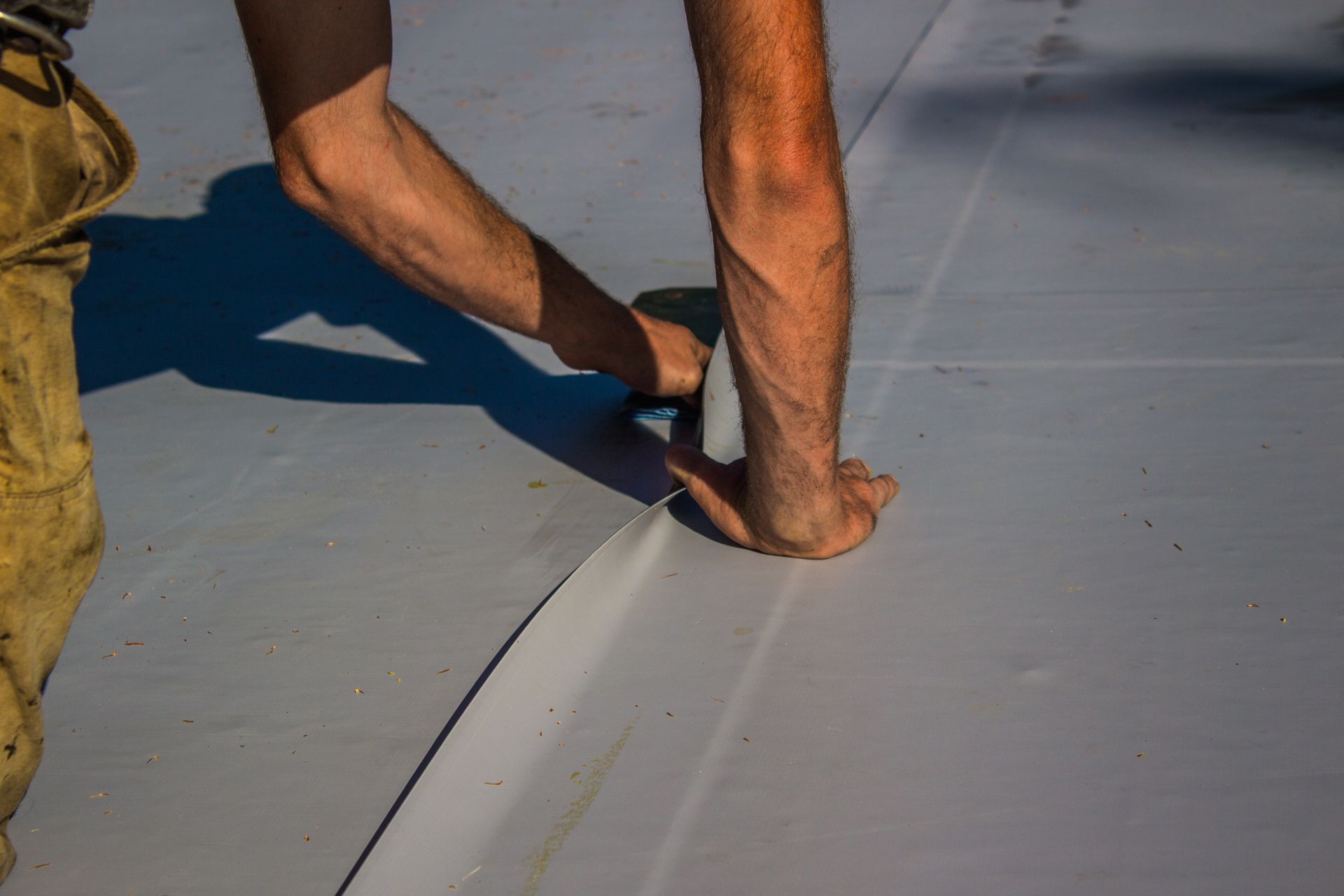 Les mains et le pied d'une personne sur une surface grise, utilisant un outil pour lisser une couture.