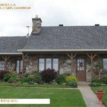 Maison en pierre avec toit gris, porche en bois et pelouse verte.