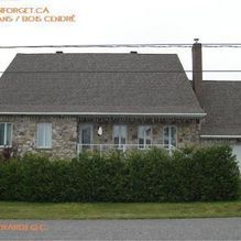 Maison en pierre avec un toit gris et une haie verte bien taillée devant.