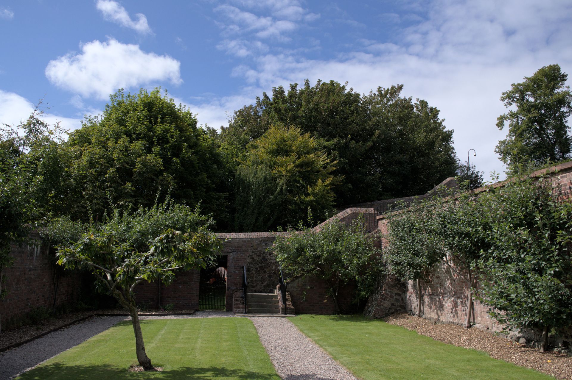 Old brick garden wall and mature trees beside a path in a period garden
