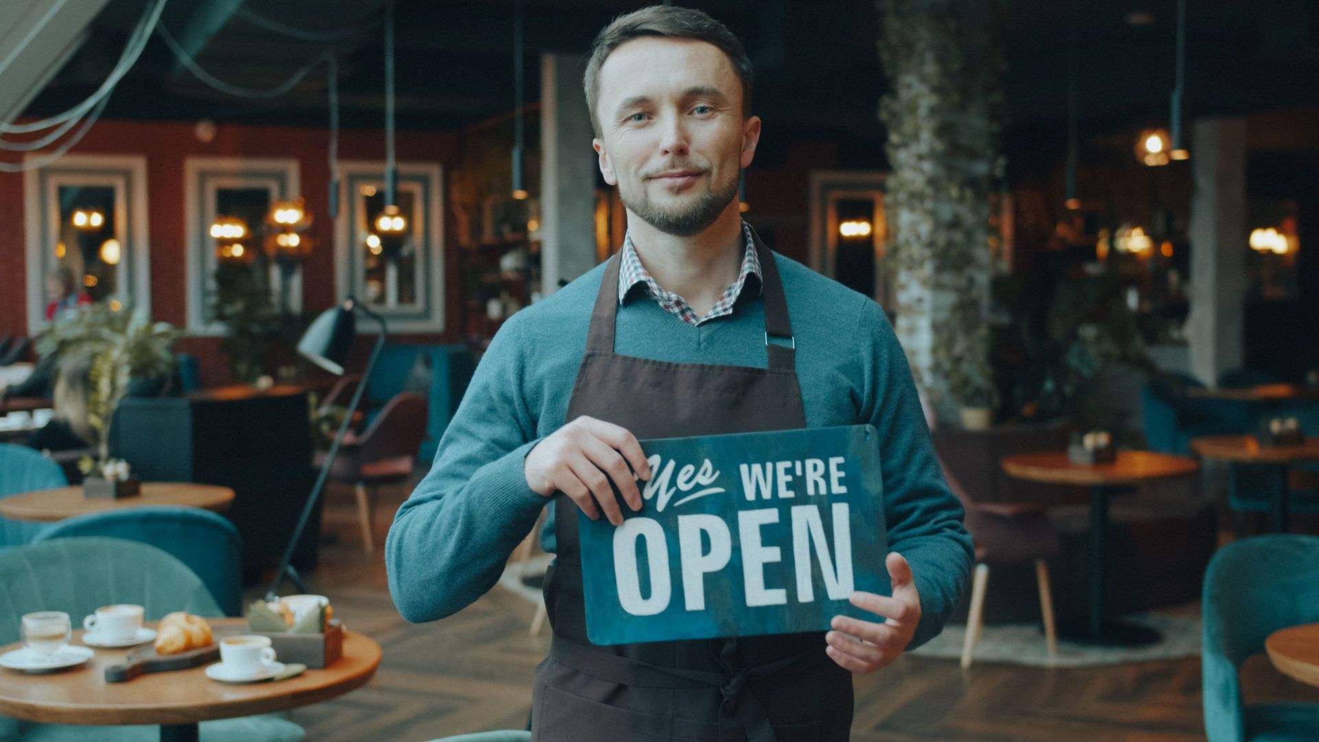 Business owner holding a We're Open sign in his cafe