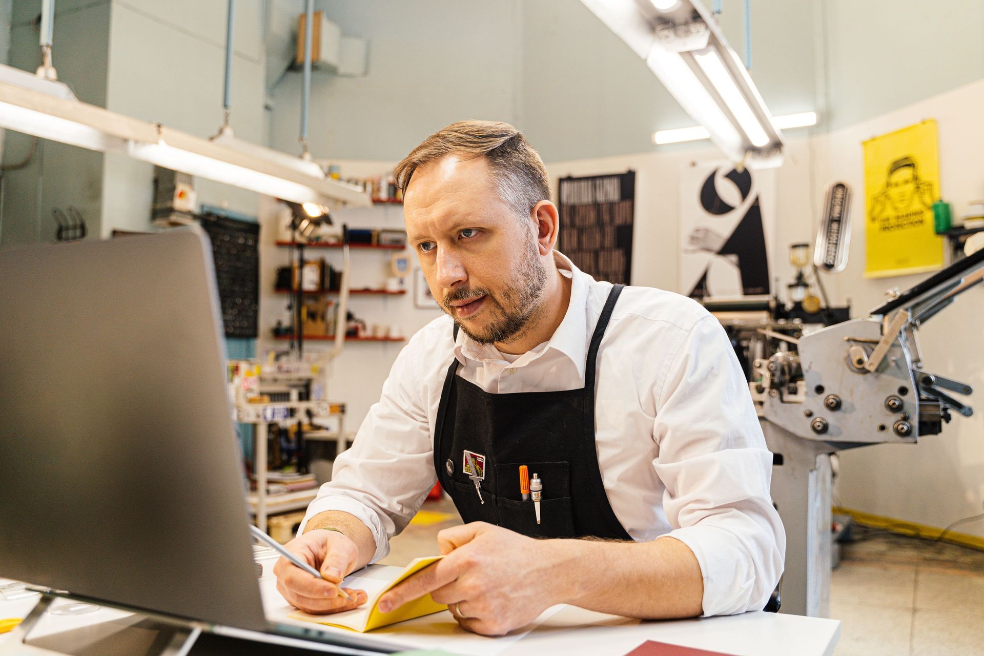 Business owner in an apron working on a laptop in his workshop