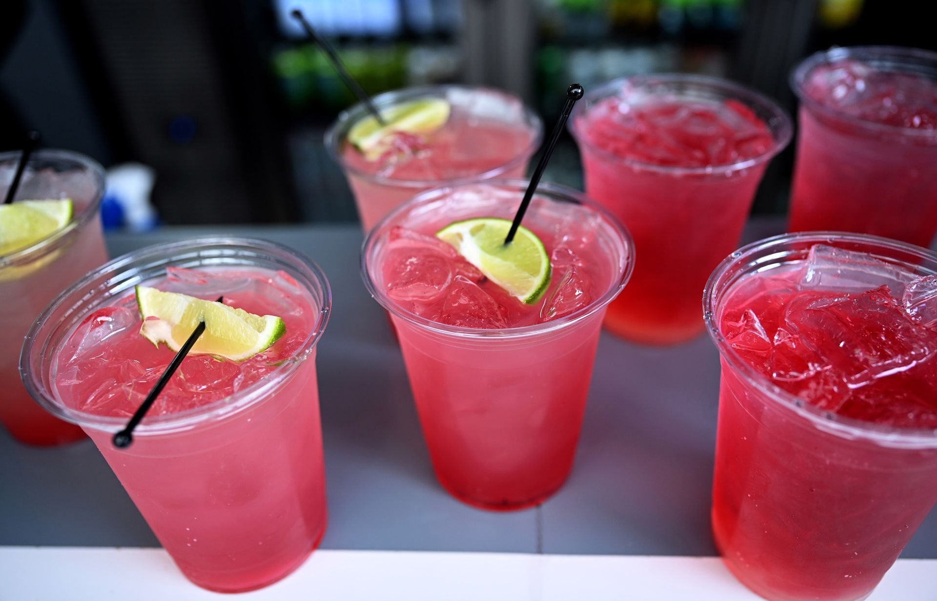 Pink drinks in clear cups, garnished with lime and straws, arranged on a counter.