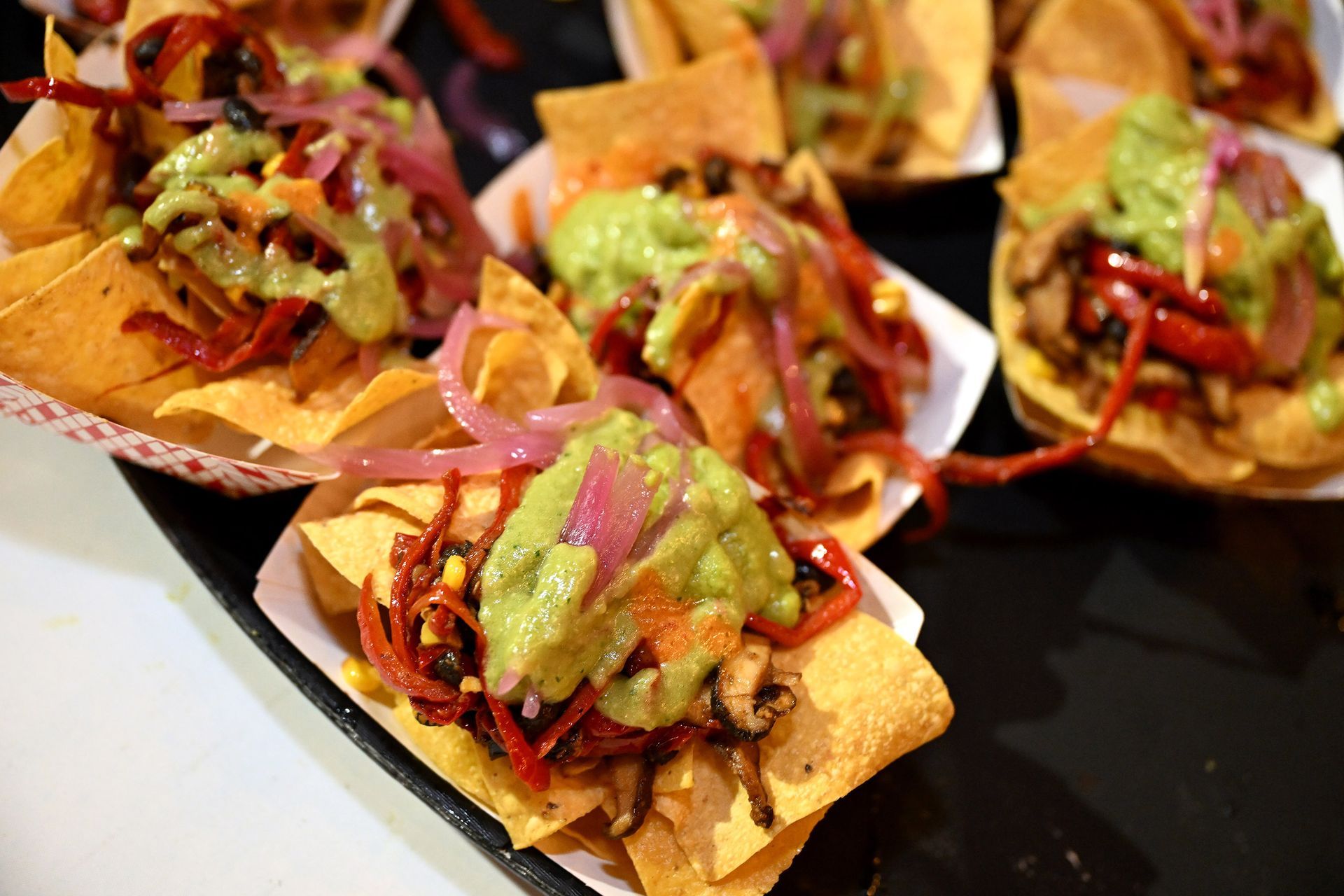 Nachos with guacamole, red onions, and toppings served in small paper containers.