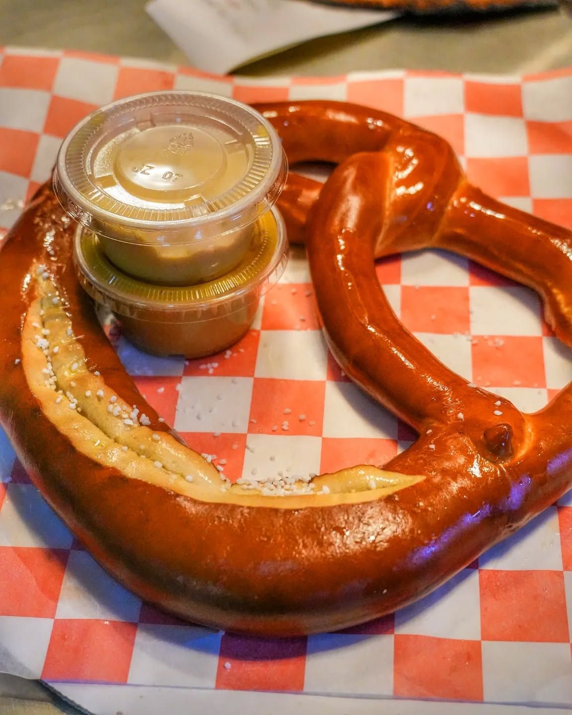 Soft pretzel with salt and mustard on checkered paper.