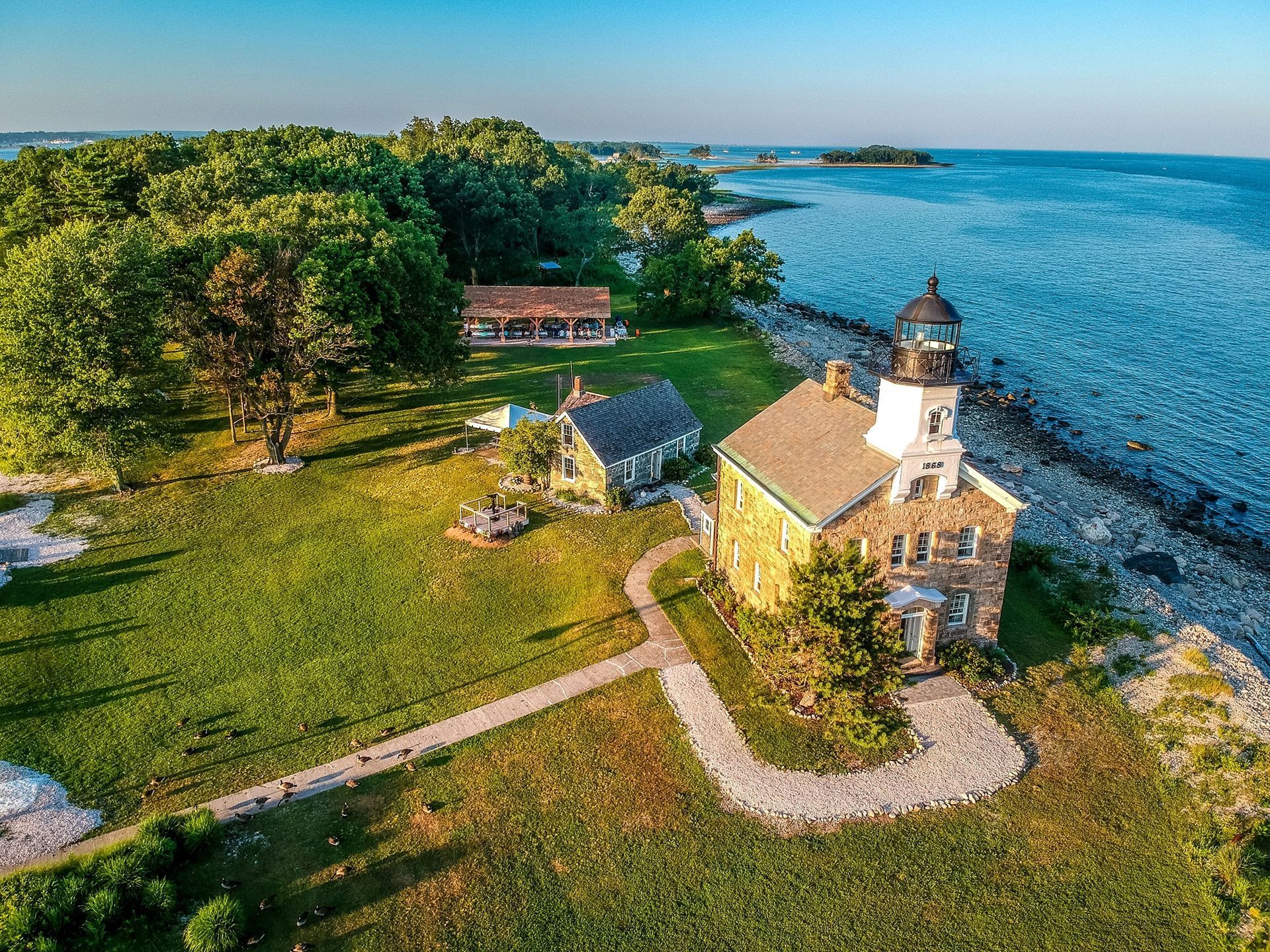 Lighthouse and buildings on a grassy shore next to a rocky coast and blue water.